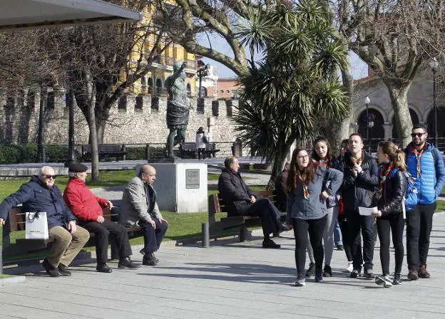 Unos jóvenes pasan por delante de varios pensionistas sentados en los bancos de la plaza de Campo Valdés, en Gijón. / JOAQUÍN PAÑEDA