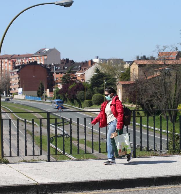 Una mujer camina por un puente con Santullano al fondo. / ALEX PIÑA